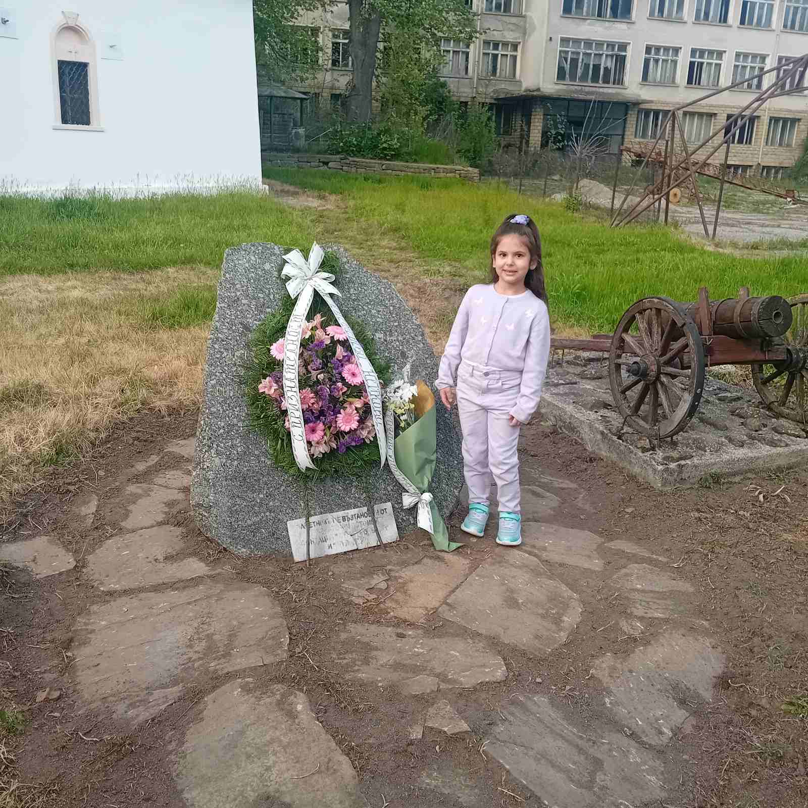 Момиче до паметник с цветя.