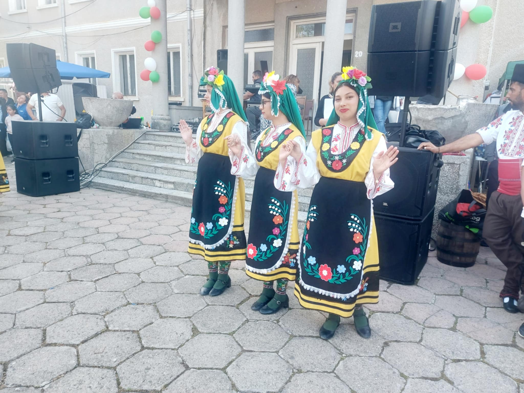 Три жени в народни носии танцуват на събитие.