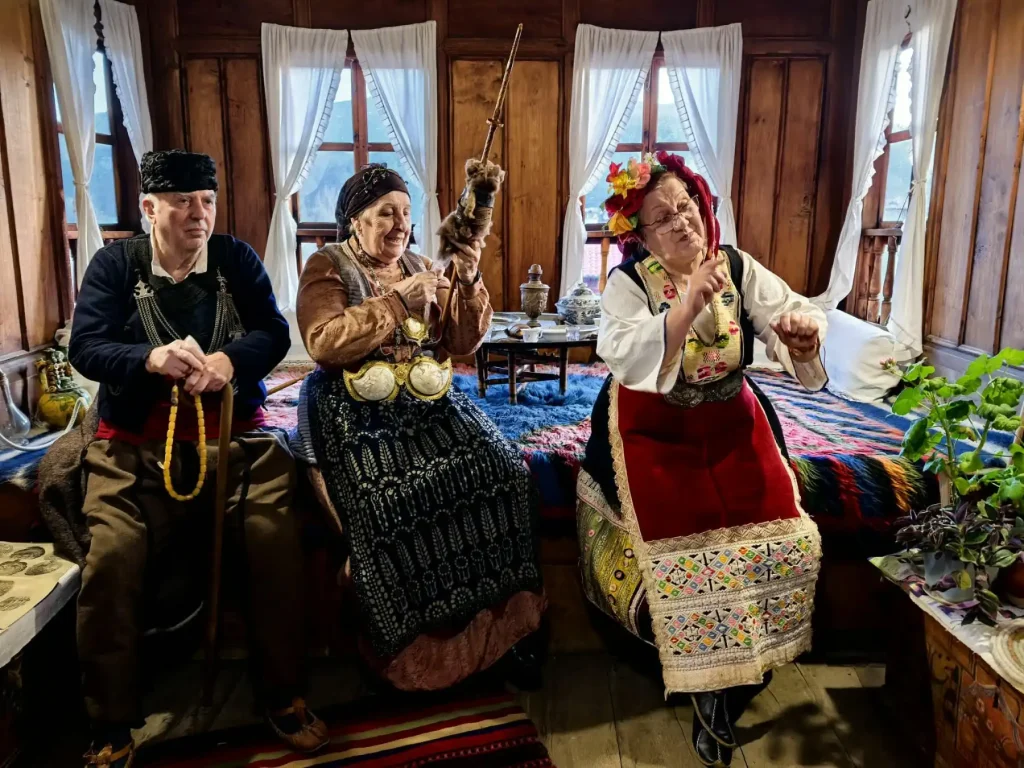 Three individuals in traditional Bulgarian costumes sit together in a wooden room, playing instruments and celebrating cultural heritage.