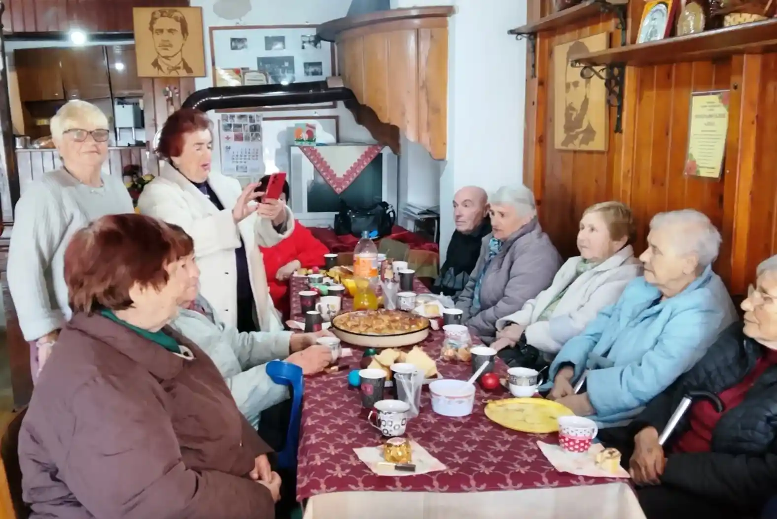 Събиране на възрастни хора в уютно заведение, наслаждават се на храна и разговори около маса.