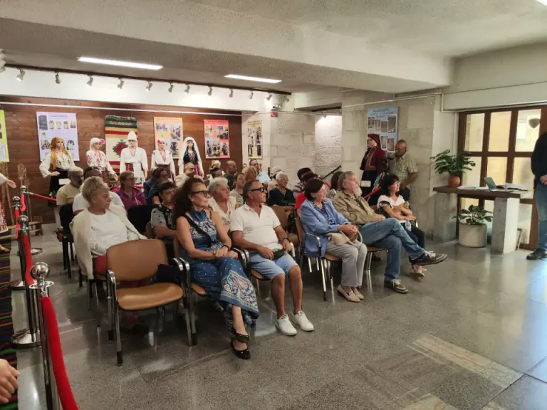Група хора, седнали в аудитория, обсъждат културно събитие с експонати на стените.