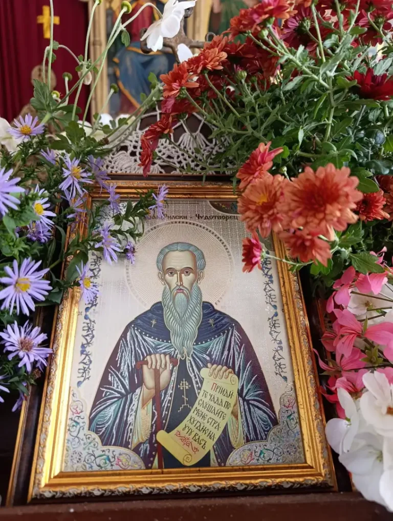 Икона на свети мъченик, обкръжена от цветя в църква, символизираща духовност и почит.