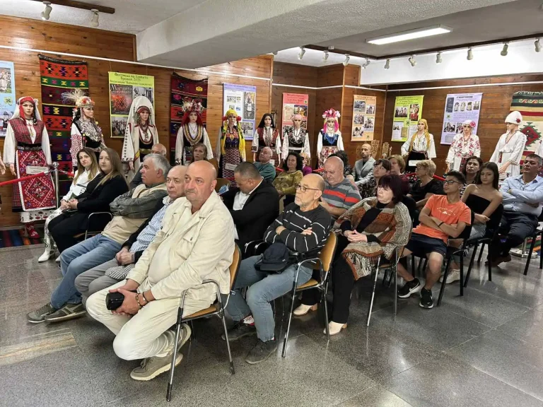 Публика на събитие, облечена в традиционни български носии, с展示 на фолклорни облекла.